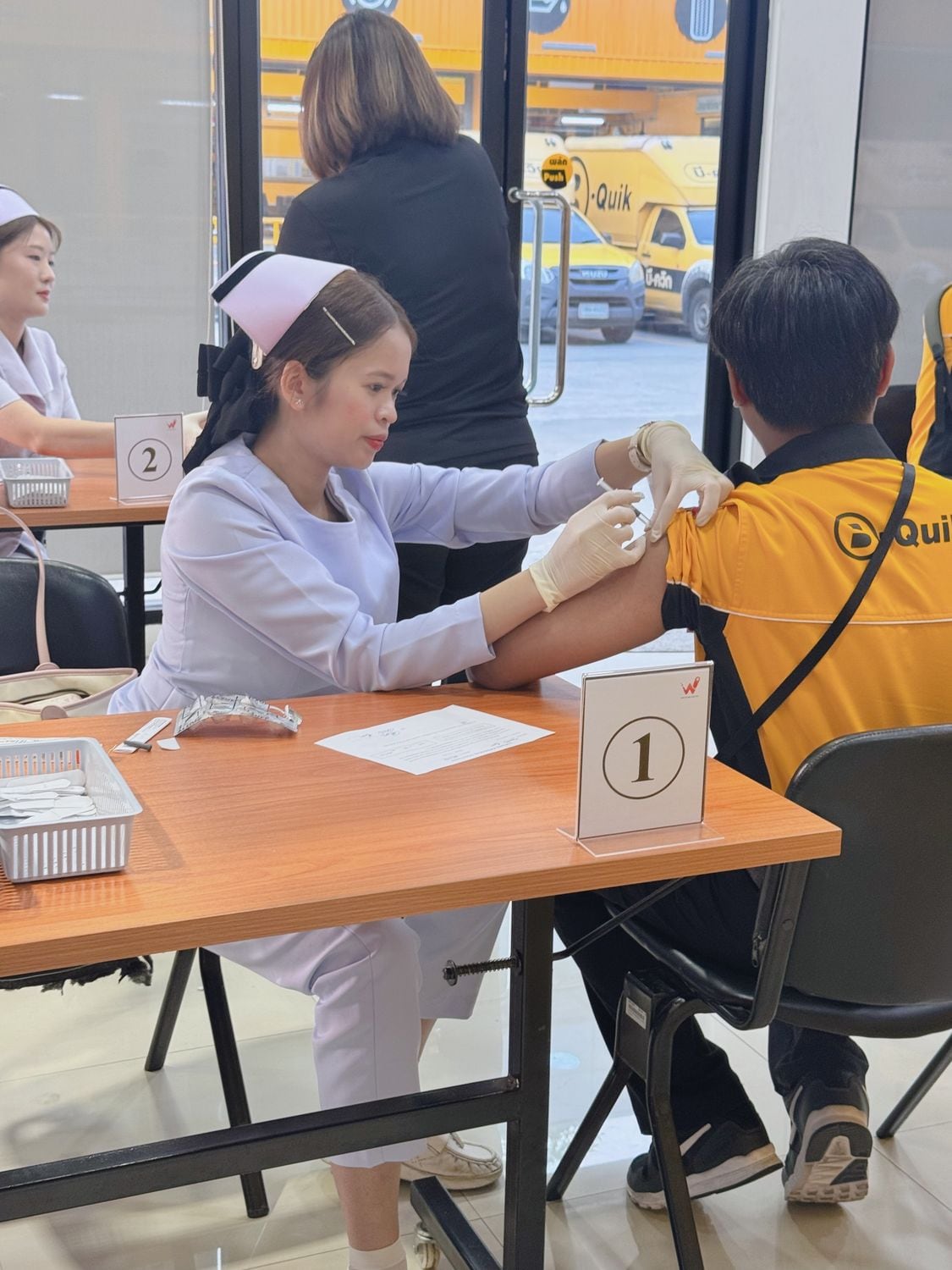 A W-Asia nurse administering a vaccine to a seated worker at station one